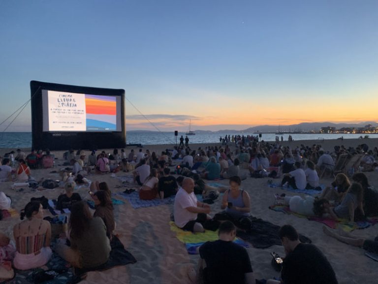 Foto de pantalla inflable con proyección, en la playa con varias personas y la puesta de sol al fondo