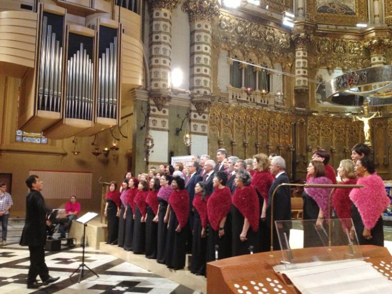 Coral musical en una iglesia. Maestro delante y el coro cantando todos con un detalle de color rojo en el cuello.