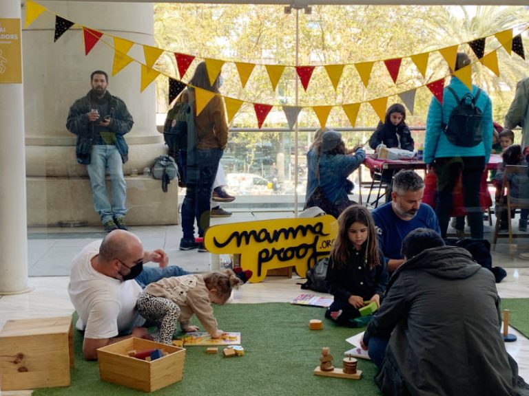 Familias con niños y niñas sentados en césped artificial, disfrutando de un festival